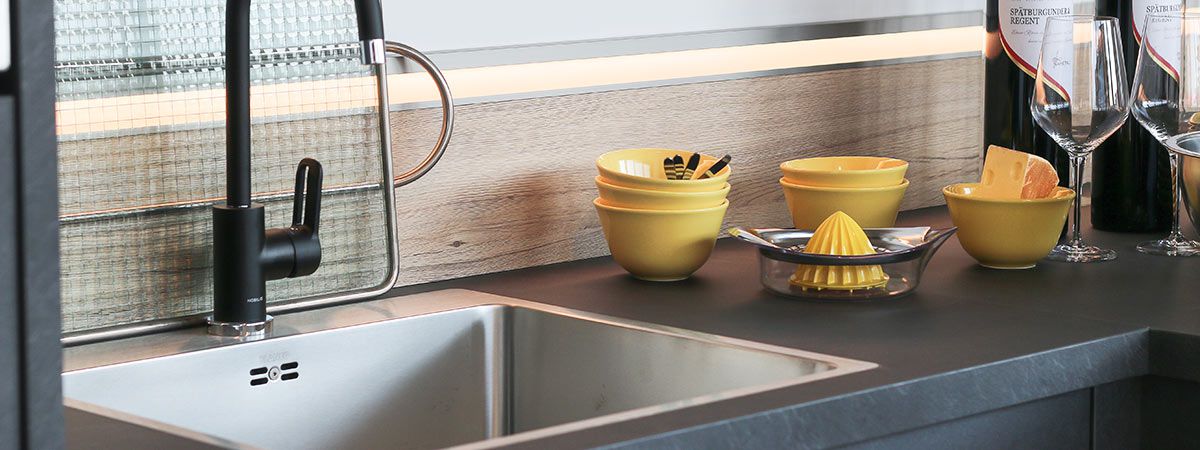 Moderne Küchenspüle mit schwarzem Wasserhahn, gelben Schalen, Zitronenpresse, Weingläsern und Weinflaschen.